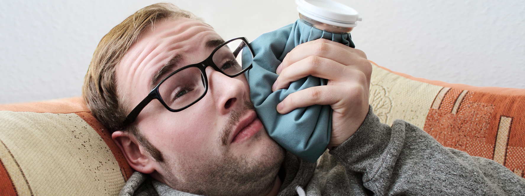 A man holding an ice pack to his jaw, likely dealing with a dental infection that leads to a root canal in Casper.